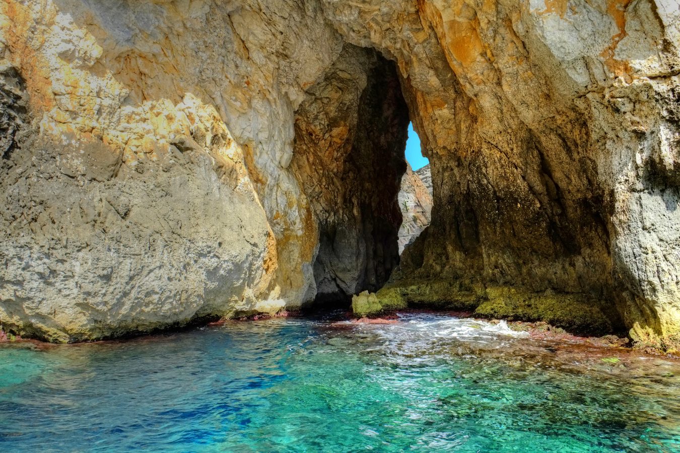 view of bright blue water of blue grotto with cliff faces in front of image