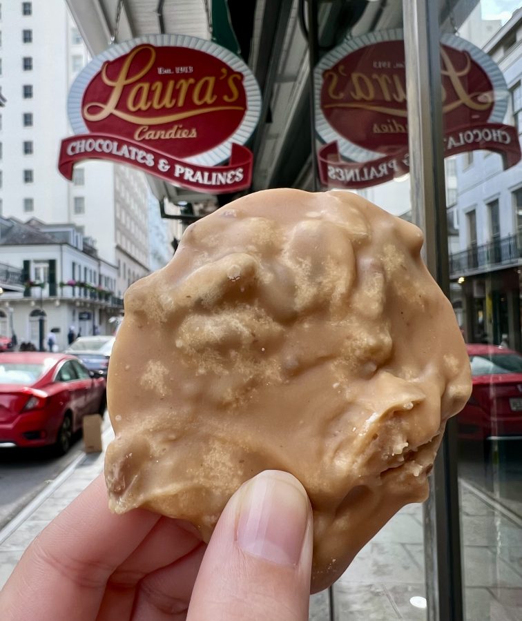 new orleans praline being held up in front of shop sign, one of the best gifts to buy new orleans souvenirs
