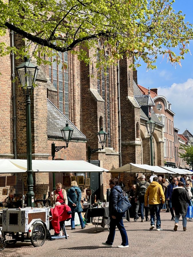 delft flea market stalls set up underneath oude kerk with people browsing through them, a fun activity during a day trip to delft from amsterdam
