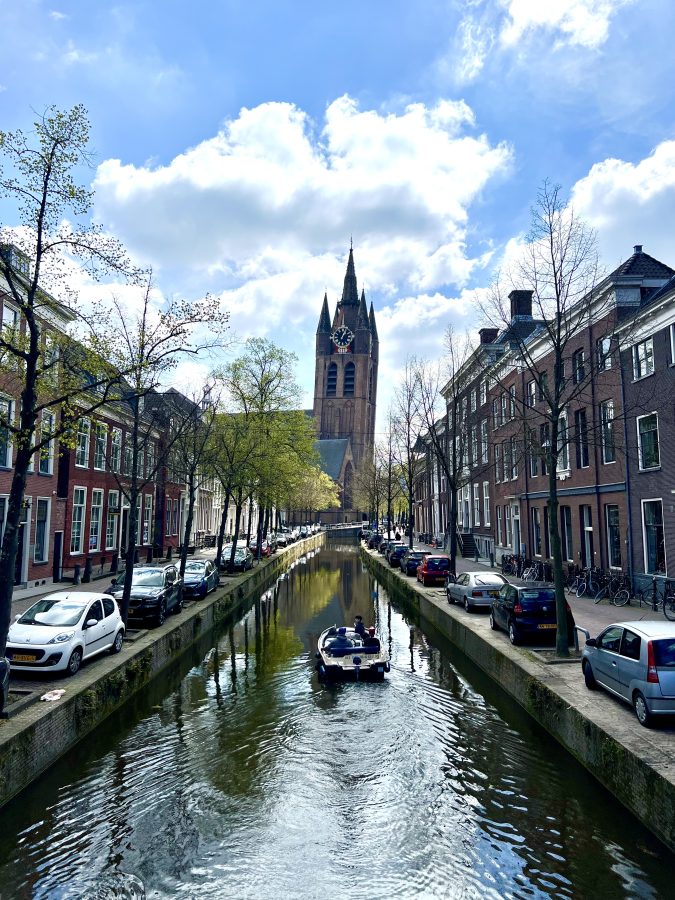 view of a canal in delft netherlands with a boat in the center and a view of the old kerk leaning tower in the distance