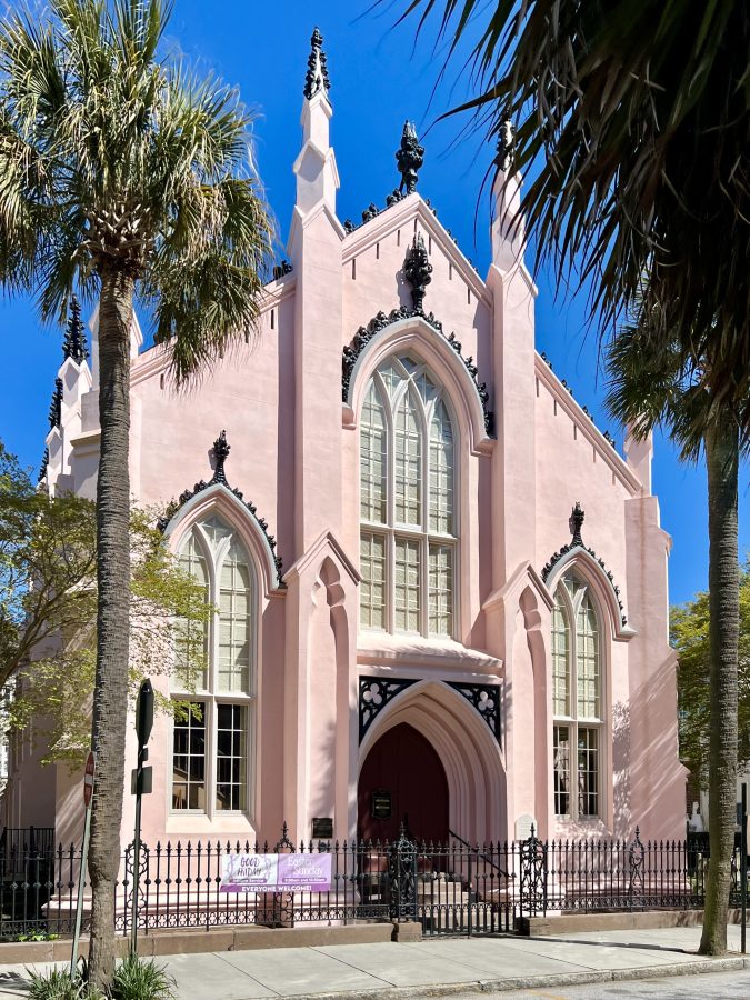 front facade of the french huguenot church in charleston, painted pink, with a palm tree visible on the left