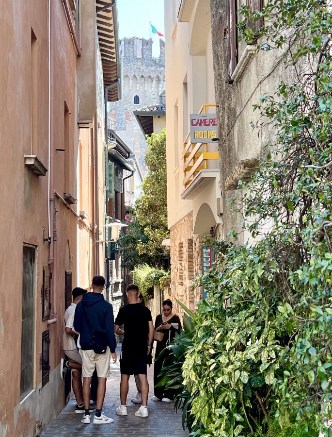 group of people hanging out on a narrow street in sirmione with castle tower visible in the distance