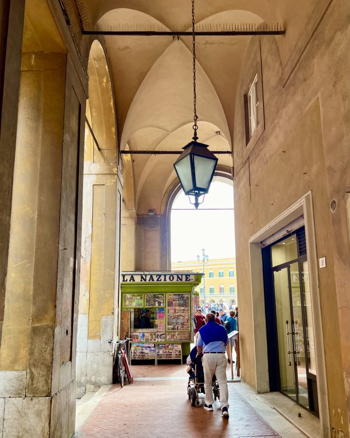 light yellow portico in pisa italy with la nazione stand at the end of it, as seen during a day trip to pisa italy