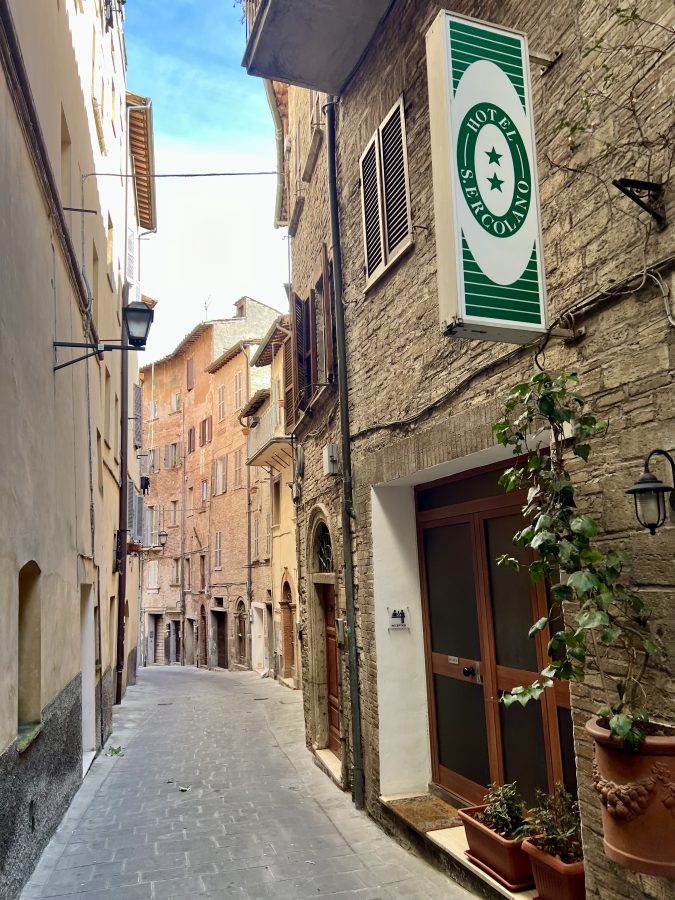 green and white sign for hotel s ercolano on an empty side street in perugia italy