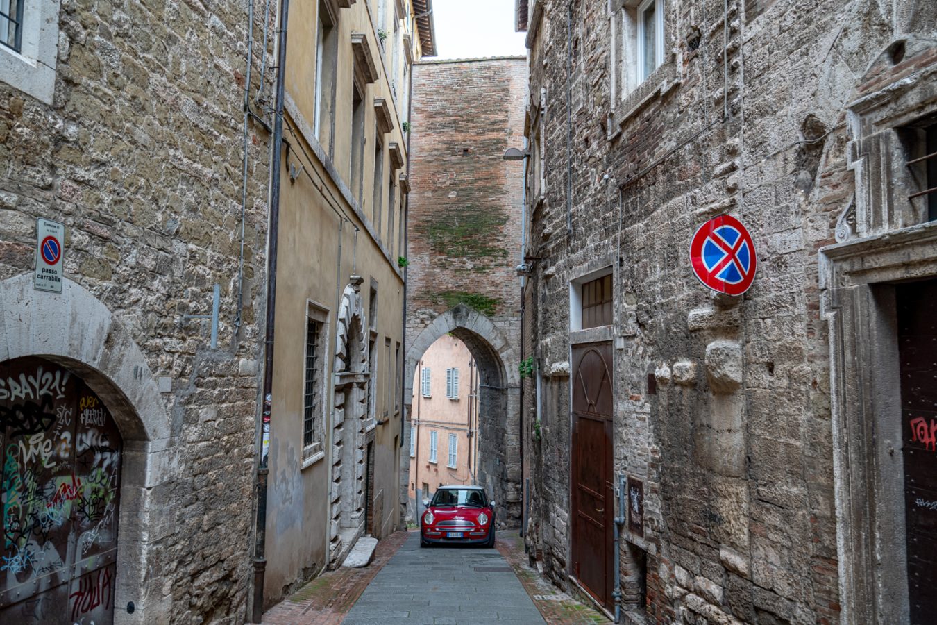 etruscan gate in perugia italy with a red fiat parked under it