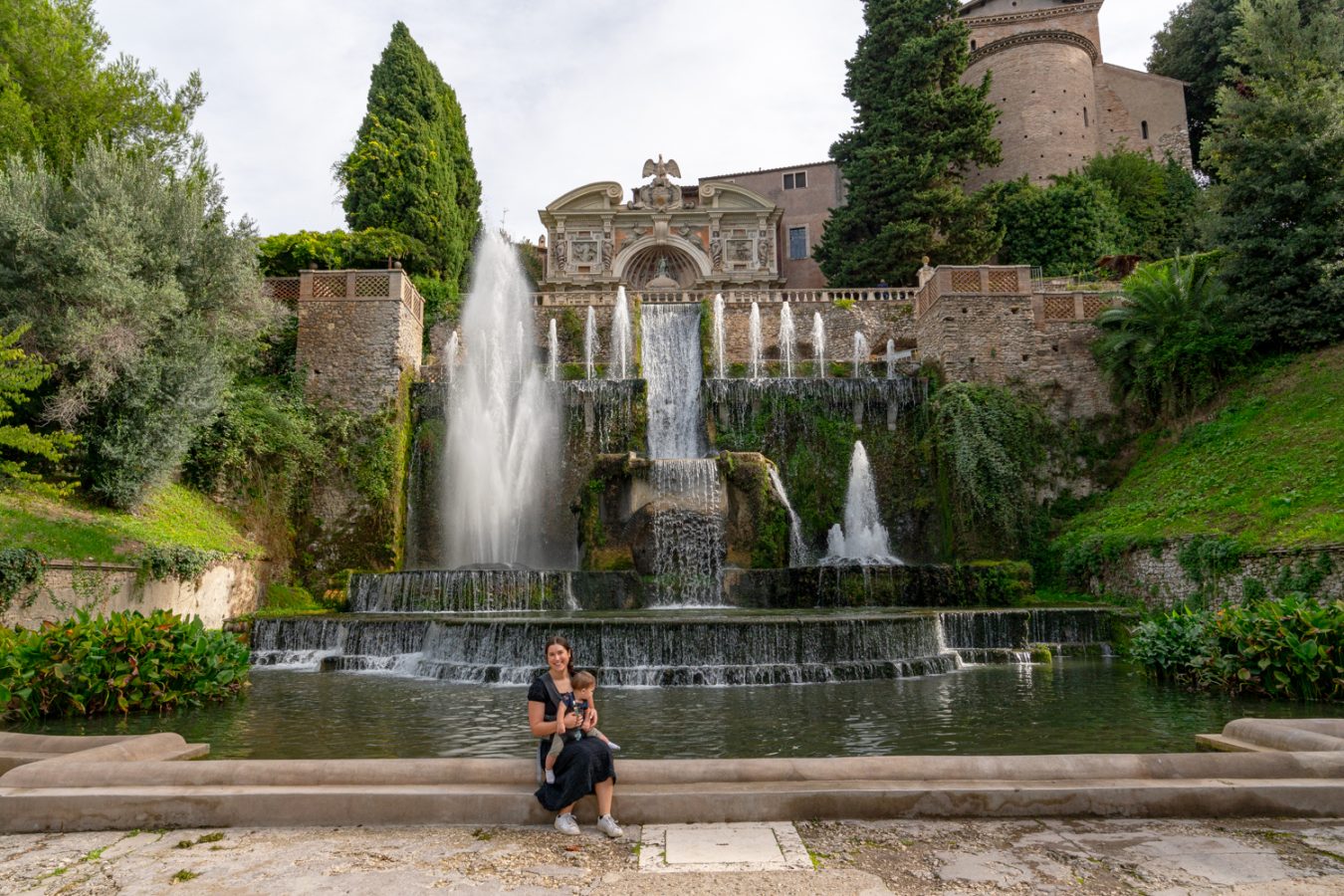 kate storm and her baby sitting at the base of the fountains of villa d'este, one of the best stops on a tivoli day trip from rome